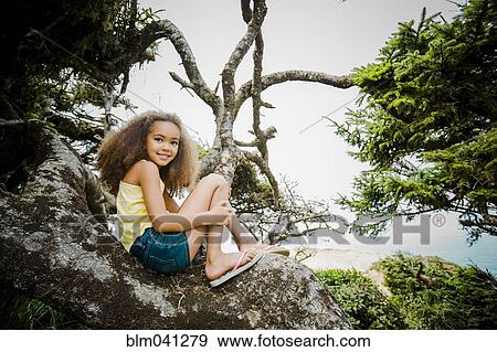 Stock Photo - Mixed race girl smiling on rock. Fotosearch