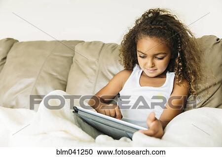 Stock Image - Mixed race girl using digital tablet on sofa. Fotosearch