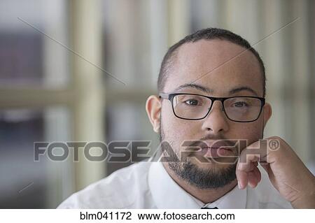 Stock Image - Mixed race man with down syndrome resting chin in hands. Fotosearch