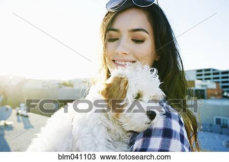 Stock Image - Mixed race woman holding dog on urban rooftop. Fotosearch