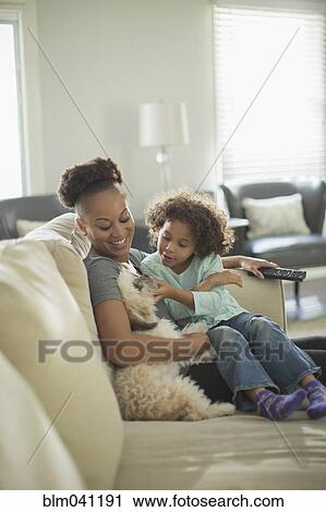 Stock Image - Mother and daughter petting dog on sofa. Fotosearch
