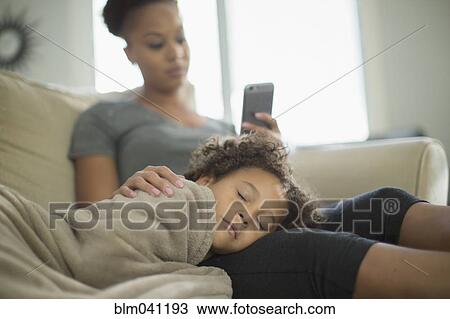 Stock Image - Mother and daughter snuggling on sofa. Fotosearch