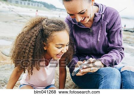 Mother and daughter using cell phone on beach View Large Photo Image Stock Photo - Mother and daughter using cell phone on beach. Fotosearch