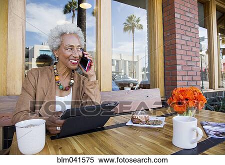 Stock Photography - Older African American talking on cell phone at cafe. Fotosearch