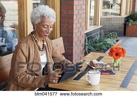 Stock Photo - Older African American using digital tablet at cafe. Fotosearch