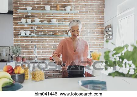 Stock Photograph - Older Caucasian woman cooking spaghetti in kitchen. Fotosearch