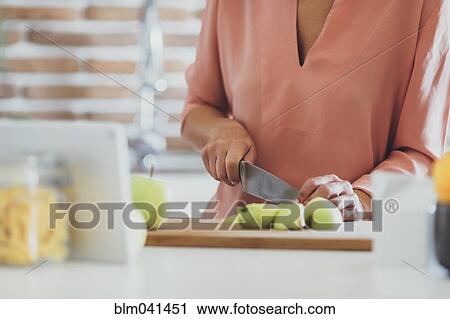 Stock Image - Older Caucasian woman cutting apples in kitchen. Fotosearch