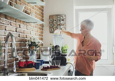 Stock Image - Older Caucasian woman making smoothie in kitchen. Fotosearch