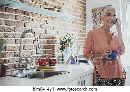 Older Caucasian woman talking on cell phone in kitchen View Large Photo Image Stock Image - Older Caucasian woman talking on cell phone in kitchen. Fotosearch