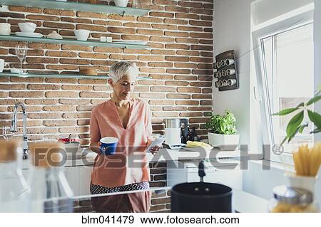 Stock Photo - Older Caucasian woman using cell phone in kitchen. Fotosearch