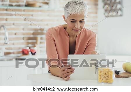 Older Caucasian woman using digital tablet in kitchen View Large Photo Image Stock Image - Older Caucasian woman using digital tablet in kitchen. Fotosearch