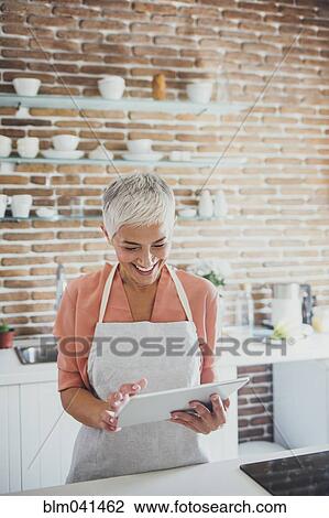 Stock Image - Older Caucasian woman using digital tablet in kitchen. Fotosearch