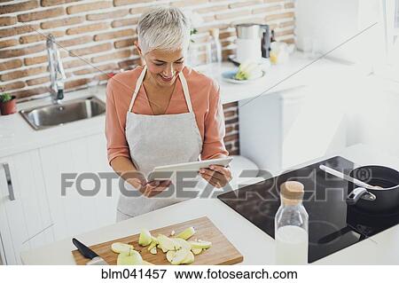 Stock Photo - Older Caucasian woman using digital tablet in kitchen. Fotosearch