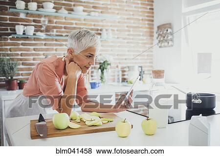 Older Caucasian woman using digital tablet in kitchen View Large Photo Image Stock Photo - Older Caucasian woman using digital tablet in kitchen. Fotosearch