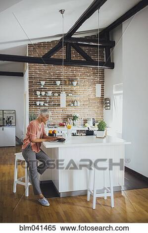 Stock Photography - Older Caucasian woman using laptop in kitchen. Fotosearch