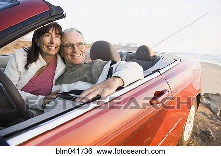 Stock Photograph - Older couple driving convertible on beach. Fotosearch