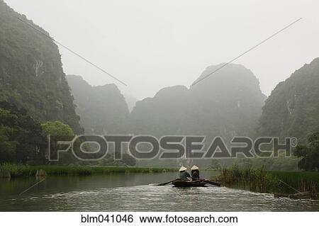 Stock Photograph - People rowing canoes near mountains in rural river. Fotosearch