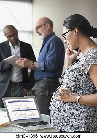 Stock Photograph - Pregnant businesswoman talking on cell phone in office. Fotosearch