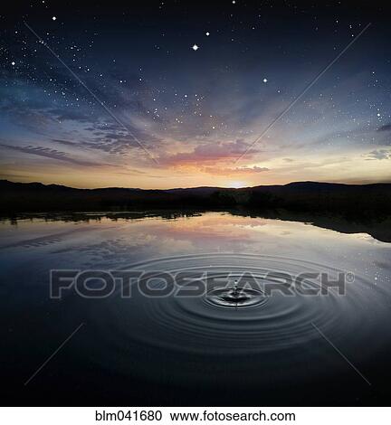 Stock Image - Ripple in rural pond reflecting sunrise sky. Fotosearch
