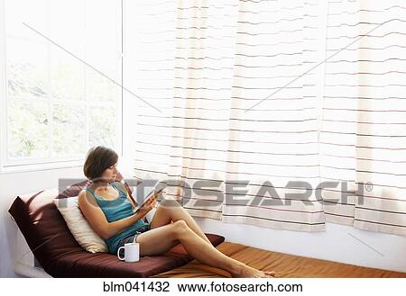 Stock Image - Woman reading book at window. Fotosearch