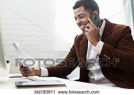 Stock Image - African American businessman talking on cell phone in office. Fotosearch