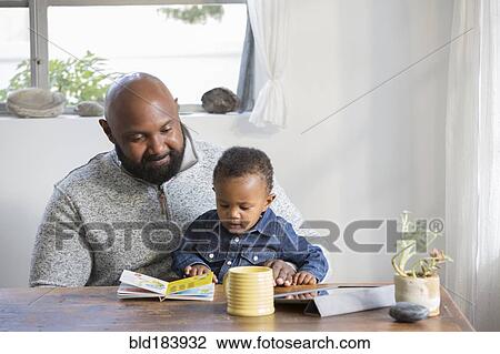 Stock Image - African American father and son reading book at table. Fotosearch