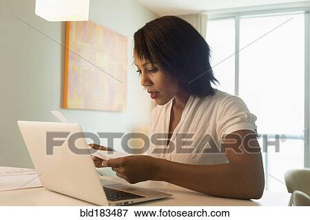 Stock Photo - African American woman paying bills on laptop. Fotosearch