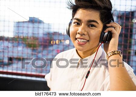 Stock Image - Asian woman listening to headphones outdoors. Fotosearch