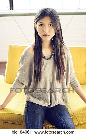 Stock Image - Asian woman sitting on yellow sofa. Fotosearch