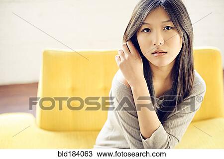 Stock Image - Asian woman sitting on yellow sofa. Fotosearch