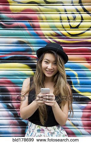 Asian woman using cell phone near graffiti wall View Large Photo Image Stock Photo - Asian woman using cell phone near graffiti wall. Fotosearch
