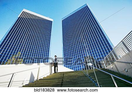 Stock Photo - Black businessman standing under highrise buildings. Fotosearch