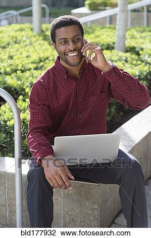 Stock Image - Black businessman talking on cell phone outdoors. Fotosearch