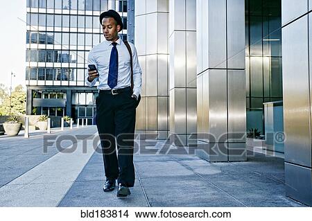 Picture - Black businessman using cell phone outside office building. Fotosearch
