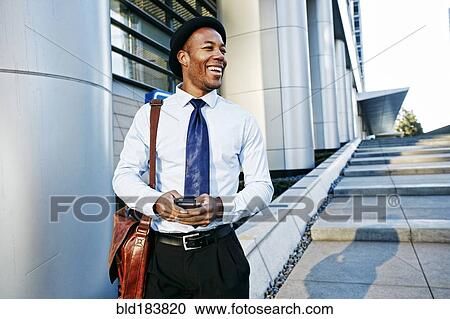 Stock Image - Black businessman using cell phone outside office building. Fotosearch