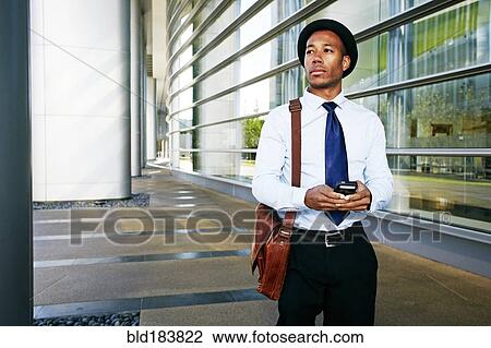 Stock Image - Black businessman using cell phone outside office building. Fotosearch