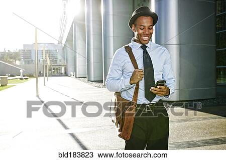 Stock Image - Black businessman using cell phone outside office building. Fotosearch