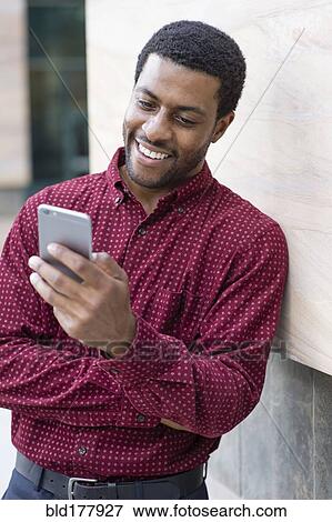 Stock Photo - Black businessman using cell phone outdoors. Fotosearch