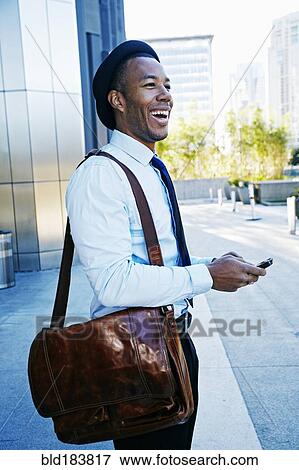 Stock Photo - Black businessman using cell phone outside office building. Fotosearch