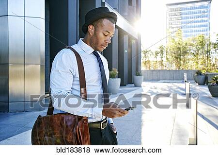 Stock Photo - Black businessman using cell phone outside office building. Fotosearch