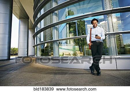 Stock Photo - Black businessman using cell phone outside office building. Fotosearch
