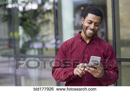 Stock Photograph - Black businessman using cell phone outdoors. Fotosearch