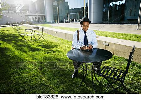 Stock Photograph - Black businessman using cell phone outdoors. Fotosearch