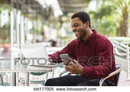 Black businessman using laptop and cell phone in cafe View Large Photo Image Stock Photography - Black businessman using laptop and cell phone in cafe. Fotosearch
