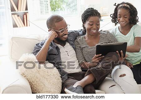 Stock Image - Black family using digital tablet on sofa. Fotosearch