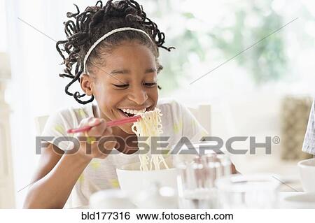 Stock Photograph - Black girl eating noodles at table. Fotosearch