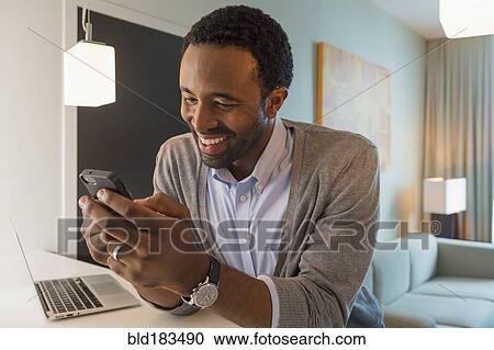 Stock Image - Black man using cell phone in living room. Fotosearch
