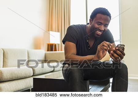 Stock Photography - Black man using cell phone in living room. Fotosearch