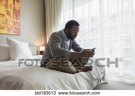 Black man using cell phone on bed View Large Photo Image Stock Image - Black man using cell phone on bed. Fotosearch