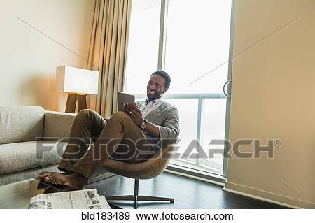 Black man using digital tablet in living room View Large Photo Image Stock Photo - Black man using digital tablet in living room. Fotosearch